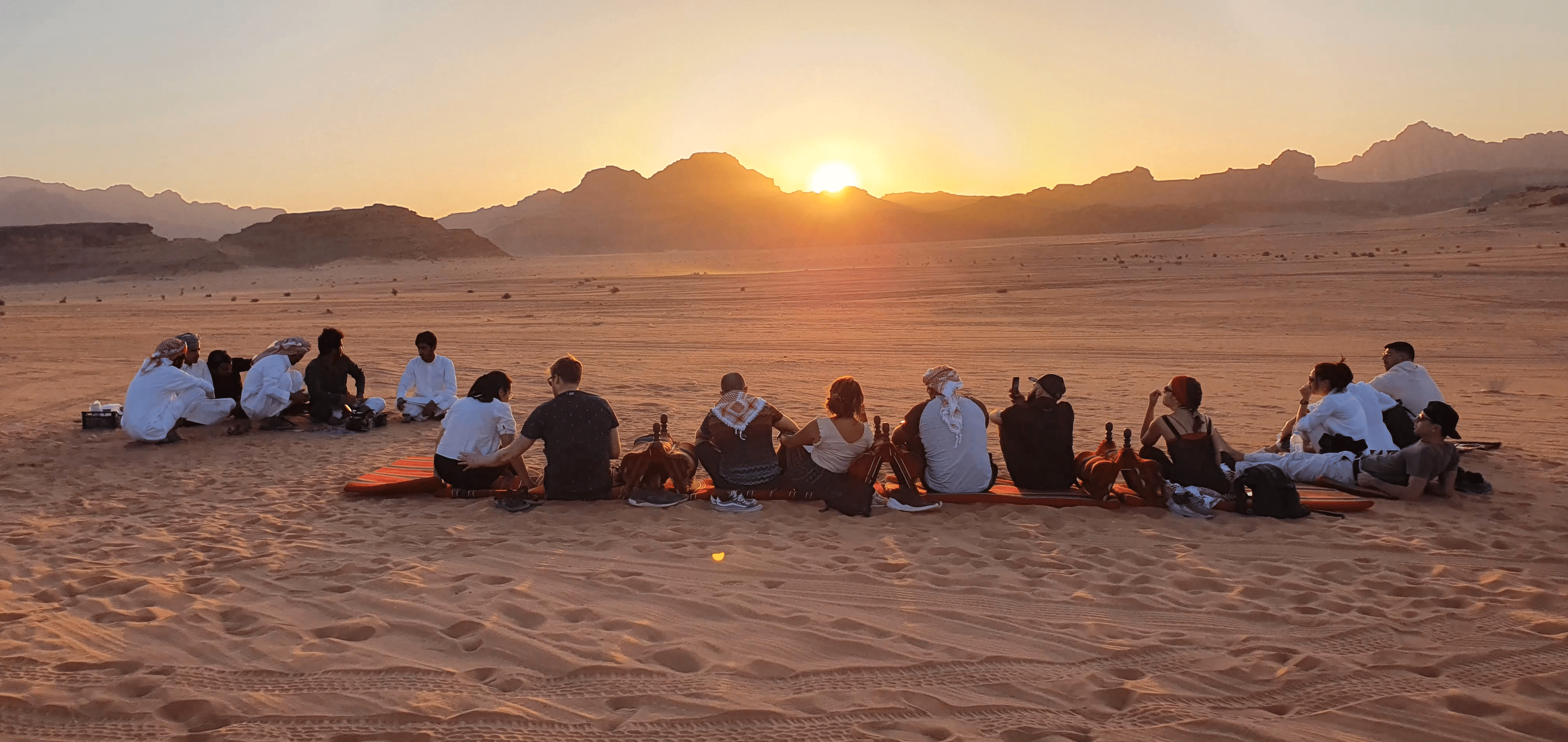 Guests gathered around a campfire at sunset in Wadi Rum